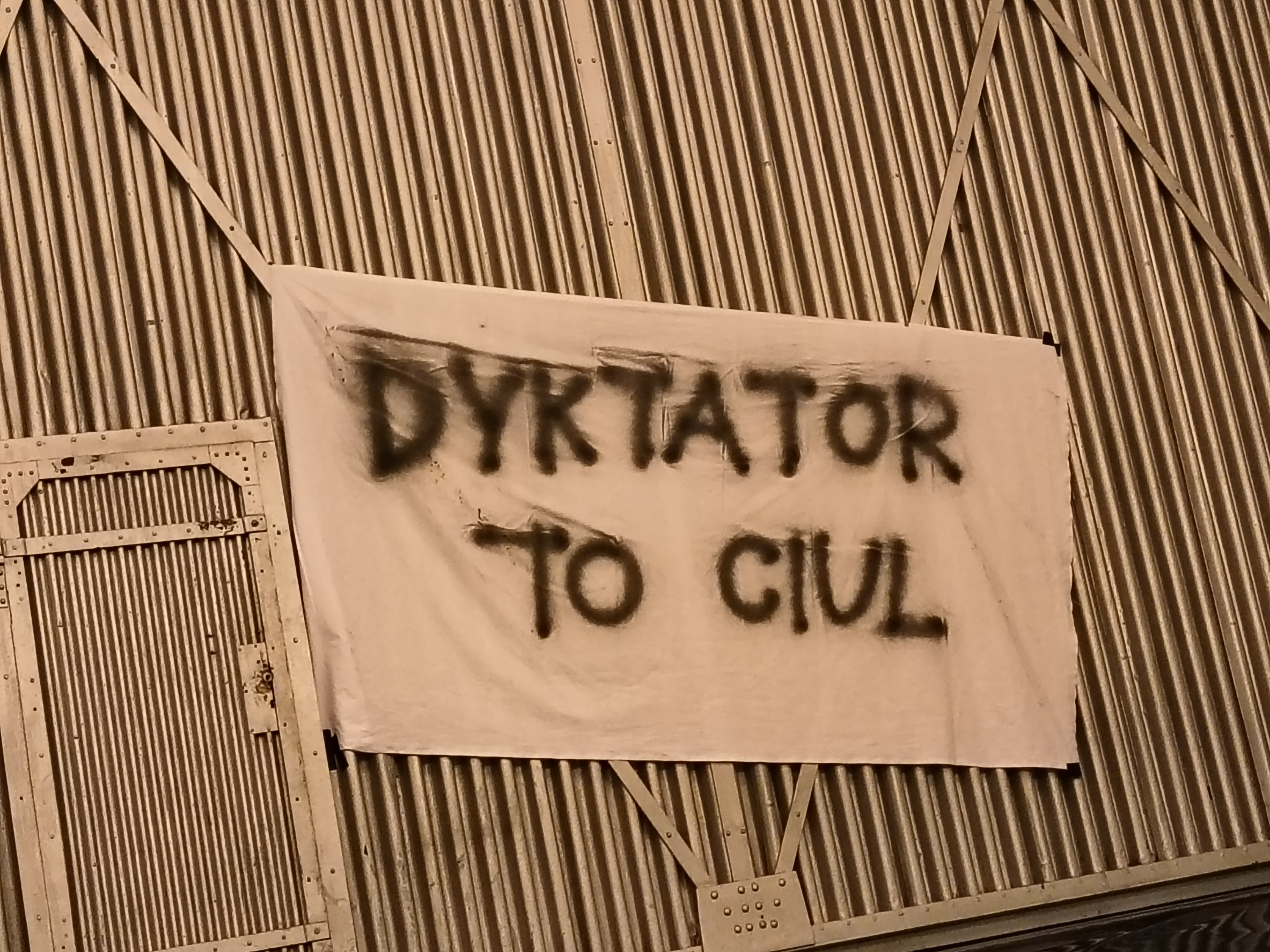 Zdjęcie kurtyny przeciwpożarowej w teatrze legnickim. Na kurtynie wisi prześcieradło z napisem Dyktator to ciul